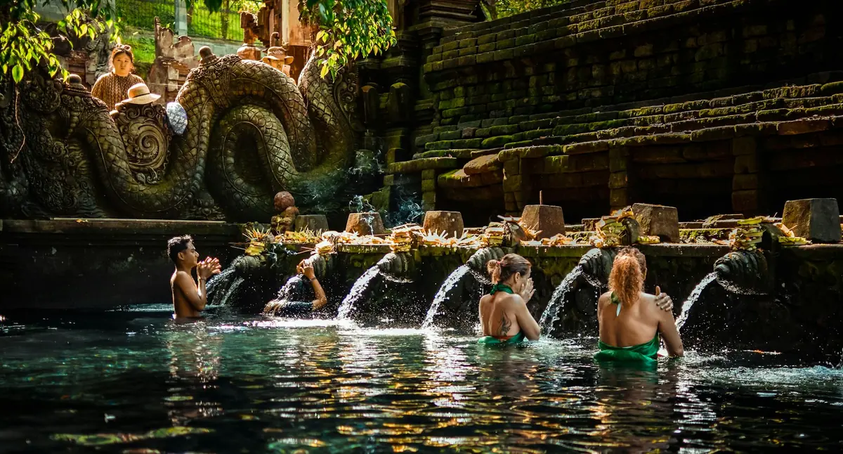 Bathers standing under the carved stone water spouts of the purification pool at Tirta Empul temple in Bali