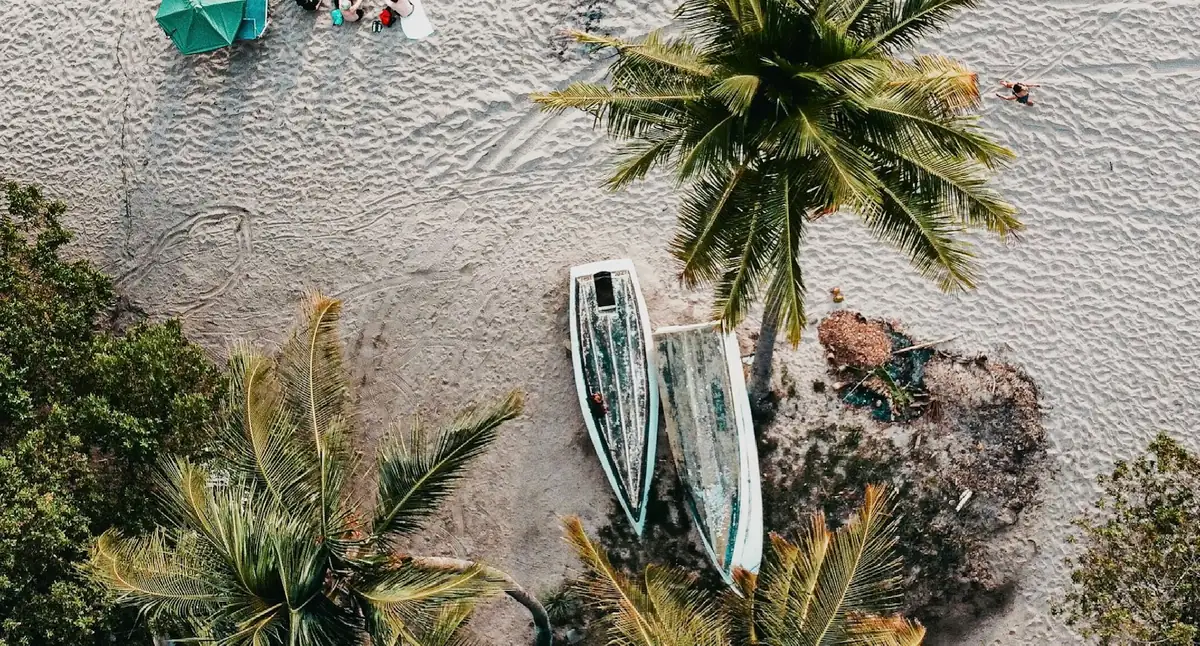 Aerial view of a sandy beach in Nosara, Costa Rica, with palm trees and two small boats pulled up on the sand