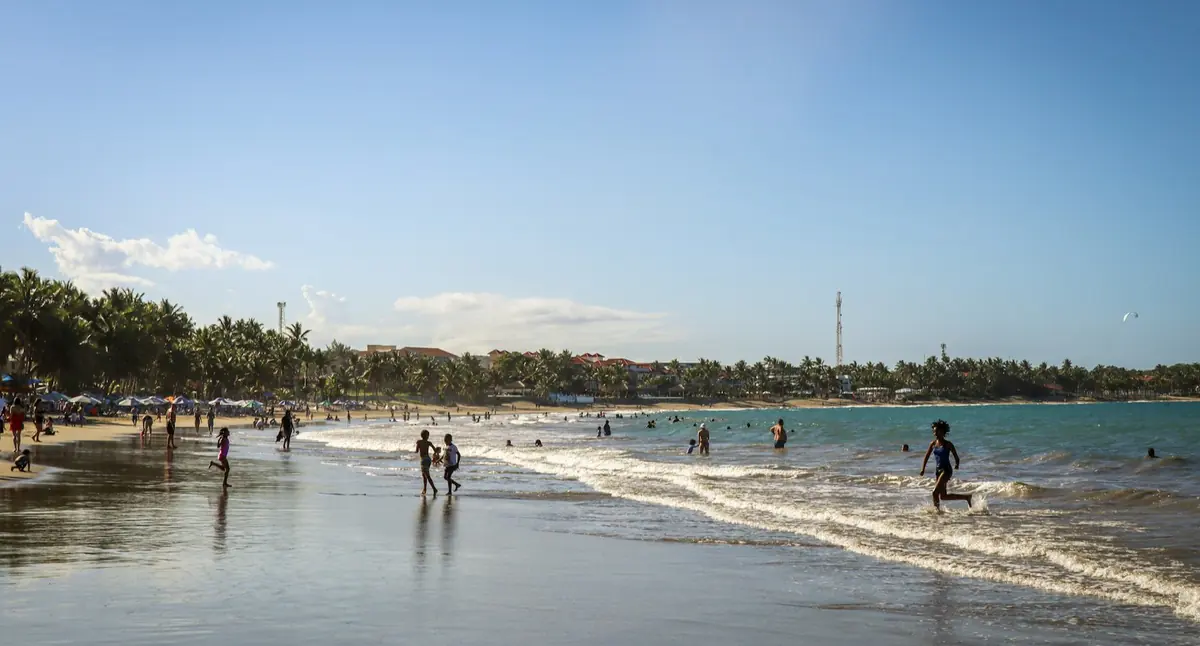Cabarete beach in the Dominican Republic, with people walking in the shallow surf and palm trees along the shoreline